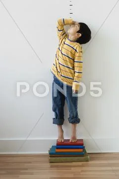 Asian boy standing on books in front of height markers Stock Photos