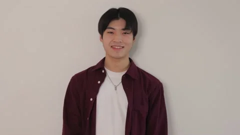 Asian boy standing still against the white wall and smiles. Medium shot. Stock Footage 220782891