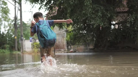 Asian boy struggles to walk across floodwater road. Stock Footage 247367491