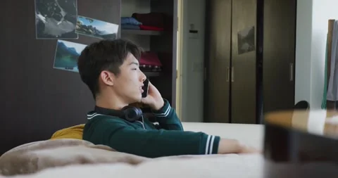 Asian boy talking on smartphone sitting on the couch at home Stock Footage 339412679