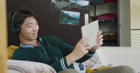 Asian boy using digital tablet sitting on the couch at home Stock Footage 339412670