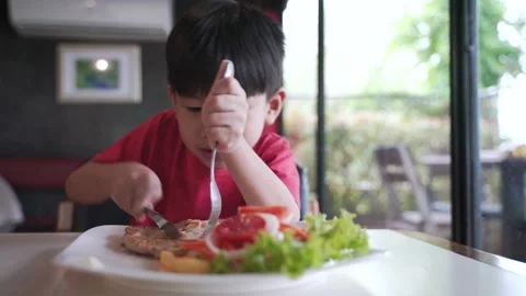 Asian boy using fork and knife for cutting steak with salad Stock Footage 152290592