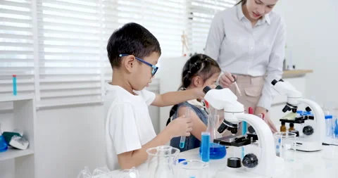 Asian boy using pipette to drop blue solution into testtube while young Asian Stock Footage 312872131