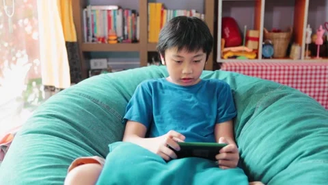Asian boy using smartphone playing game while sitting on the couch at home Stock Footage 191879617