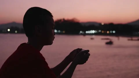 An Asian boy is using a smartphone with a sunset sky in the background. Stock Footage 145125637