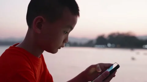 An Asian boy is using a smartphone with a sunset sky in the background. Stock Footage 145125638