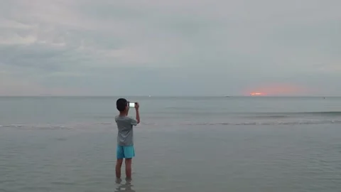 An Asian boy is using a smartphone to taking a picture of sunrise. Stock Footage 140522299
