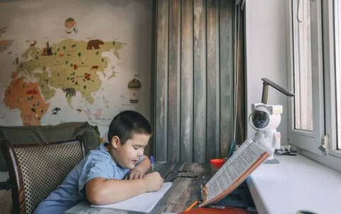 Asian boy write in notebook during homework session with geography wall map Stock Photos