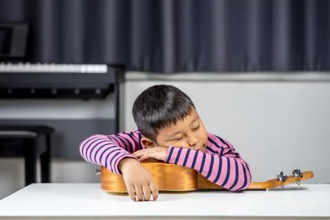 Asian boys aged 7-8 put their heads on the ukulele in the room. Stock Photos