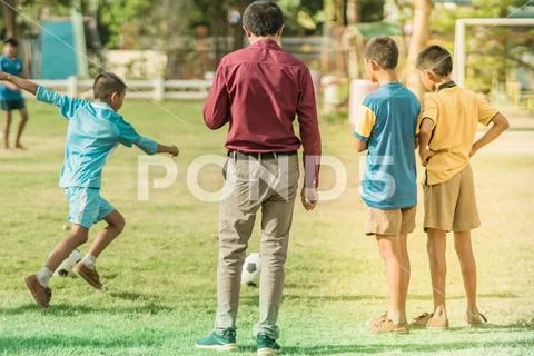 Asian boys practice kicking the ball to score goals in the public football fi Stock Photos