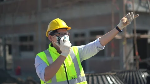 Asian builder in hard hat wearing protective face mask talking by walkie talk Stock Footage 146443473