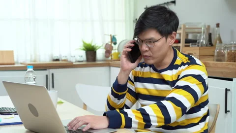 Asian business man using laptop talking on cell phone working at home . Asi.. Stock Footage 252818280