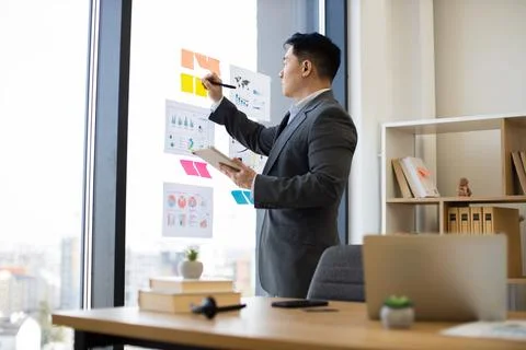 Asian businessman analyzing graphs on window with digital tablet Stock Photos