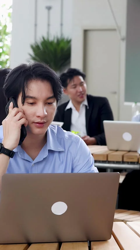 Asian Businessman Calling on Smartphone While Working on Laptop in Office Stock Footage 346664476
