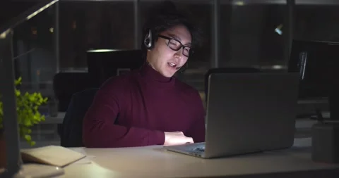 Asian businessman in headset working with computer late at night in client Stock Footage 147386728