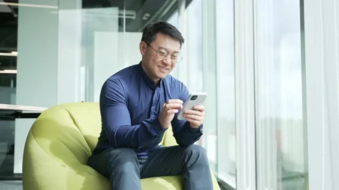Asian businessman IT programmer sits on bean bag chair hold smartphone scrolling Stock-Footage 225745416