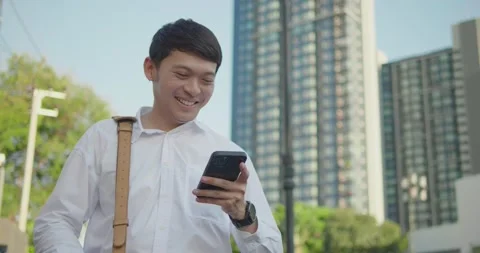 Asian businessman looking at cellphone while walking on the street Stock Footage 168725355