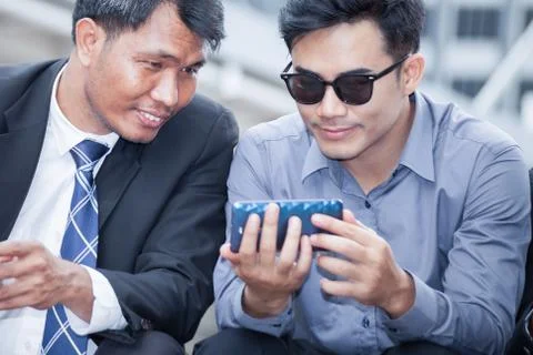 Asian businessman sitting and looking at smartphone that his colleagues pre.. Фото