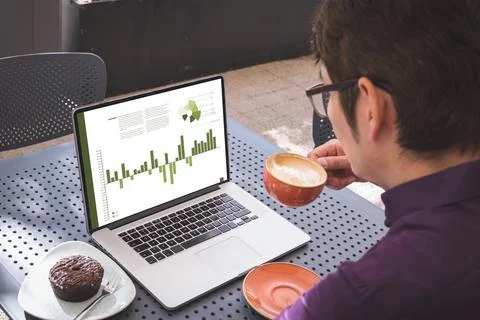 Asian businessman at table in cafe using laptop with charts and data on screen Stock Photos