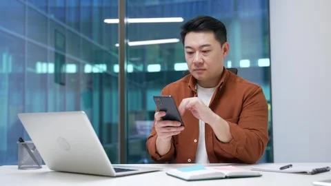 Asian businessman is using browsing mobile phone while sitting at workplace  Stock Footage 291542496