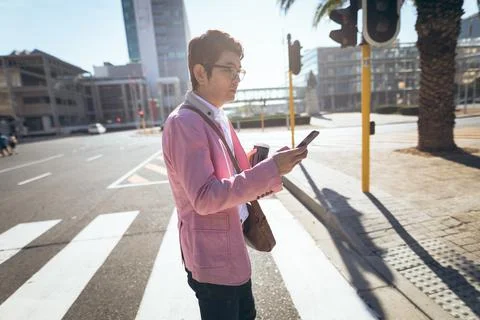 Asian businessman using smartphone drinking takeaway coffee crossing city street 写真素材