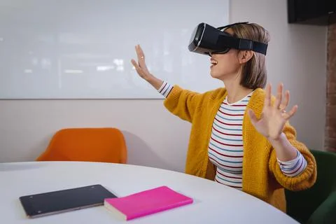 Asian businesswoman sitting at work wearing virtual reality set and playing Stock Photos
