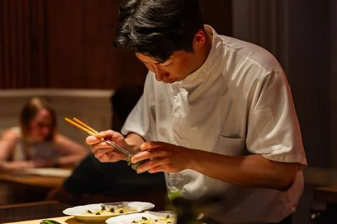 Asian chef preparing sushi with precision in restaurant Фото