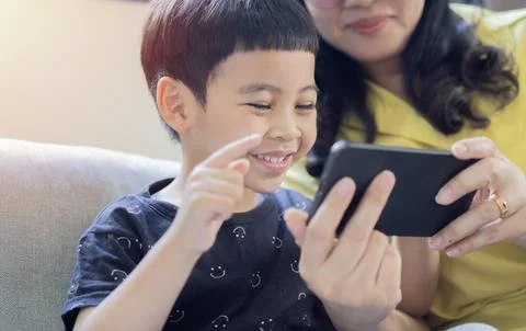 Asian child boy playing, using phone on sofa while parent sitting nearby at.. Stock Photos