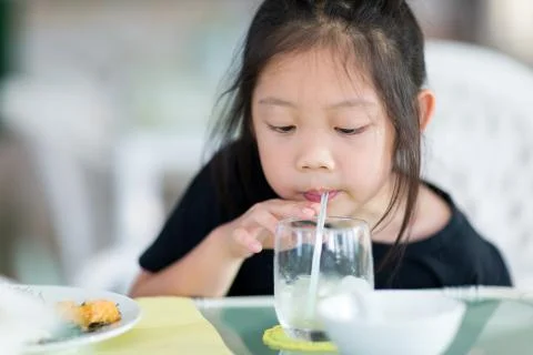 Asian Child Drinking Water Using Straw from Glass Foto stock