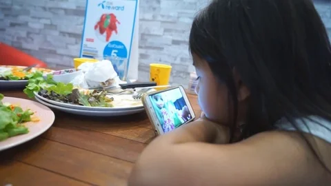 Asian Child looking smartphone wait Eating Green Salad, Girl Eats Breakfast Stockbeeldmateriaal 81368288