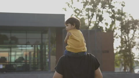 The Asian child rides on his father's back for a walk in the middle of the playg Stock Footage