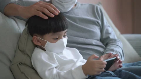 Asian child wearing mask while play game in smartphone with father Video stock 133630946