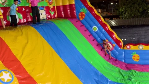 Asian Children Sliding Down a Large Inflatable Rainbow Slide at Night Stock Footage 327446636