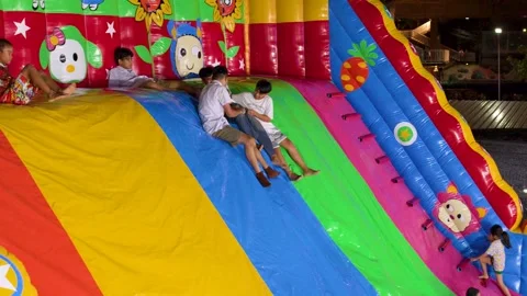 Asian Children Sliding Down Large Colorful Inflatable Slide at Night Carnival Stock Footage 327631131