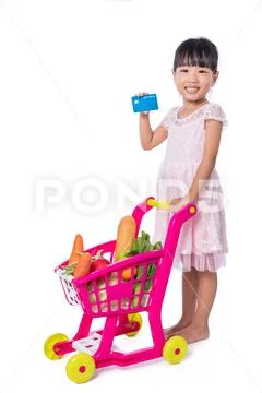 Asian Chinese little girl holding credit card with shopping trolley full of.. Stock Photos