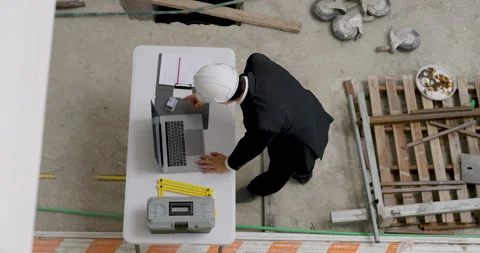 Asian construction inspector crouches over floor plan near building material, Vídeo Stock 336536629
