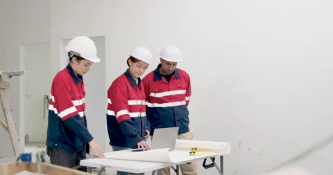 Asian construction team in red safety uniform reviews blueprint on worktable, Stock Footage 342226756