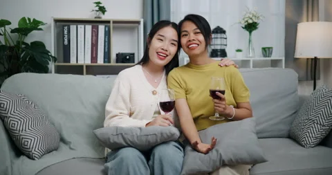 Asian couple happily chatting while relaxing on the sofa together. Stockbeeldmateriaal 316873193