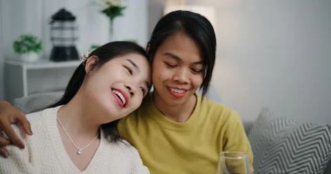 Asian couple happily chatting while relaxing on the sofa together. Stockbeeldmateriaal 316873304