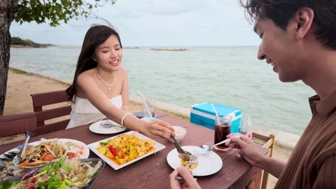 Asian Couple Having Lunch at a Beachfront Restaurant Table Stock Footage 346675897