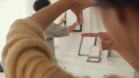 Asian couple help each other decorate new space put photo frame on wall. Stock Footage 232652401
