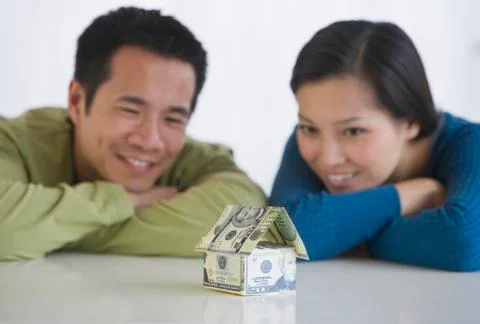Asian couple looking at house made of money Stock Photos