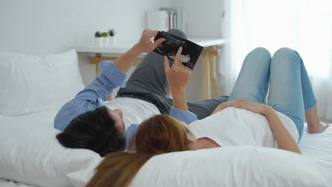 Asian couple lying down looking at the ultrasound results of their baby Stock Footage 246008389