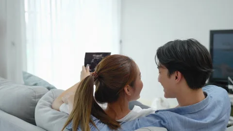 Asian couple lying down looking at the ultrasound results of their baby Stock Footage 246008800