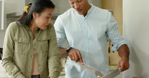 Asian couple sharing gentle touch, slicing bread and plating eggs at counter, Stock Footage 335568473
