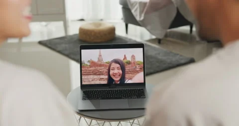 Asian couple sit on couch looking at laptop screen talk video call with friends. Stock Footage 229703183