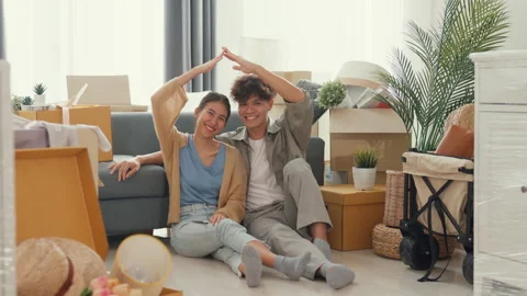Asian couple sit on sofa couch smile looking at camera making house sign. Stock Footage 232613733