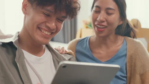 Asian couple sit on sofa couch use digital tablet online shopping at home. Stock Footage 232684300
