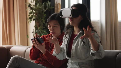 Asian couple testing VR game, happy woman exploring virtual reality simulation Stock Footage 330401982
