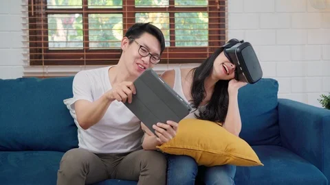 Asian couple using tablet and virtual reality simulator playing games at home. Stock Footage 108456226
